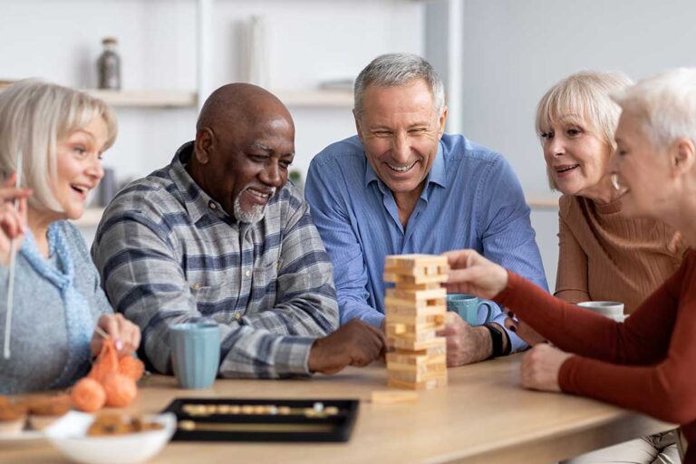 Older adults participate in gentle seated exercises together in a bright assisted living activity room.