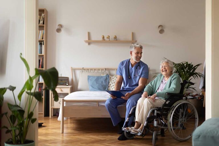 A social worker sits with two older adults in a comfortable lounge, actively listening and holding a notepad.
